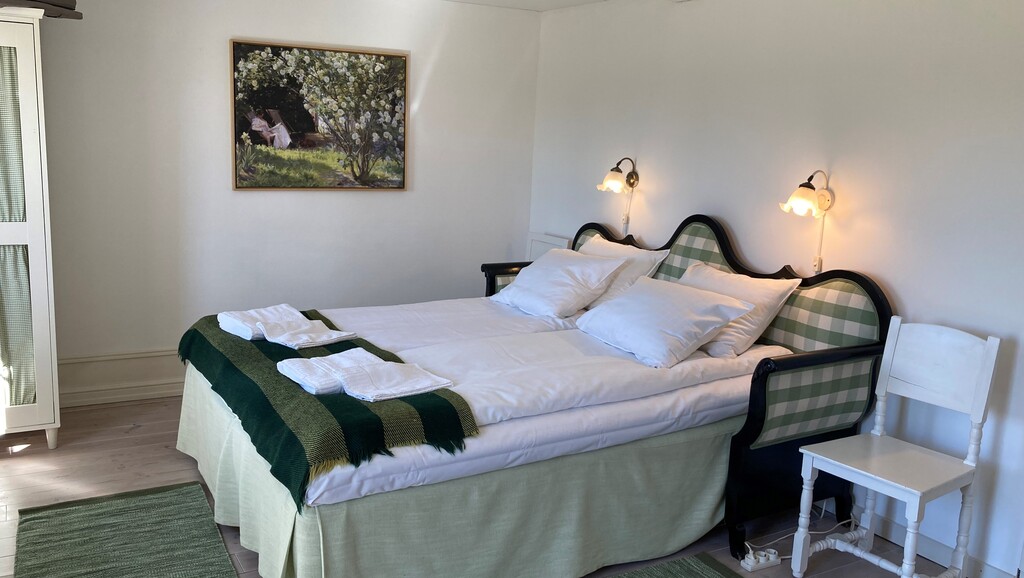 Bäddad dubbelsäng med tända sänglampor och en naturtavla på väggen