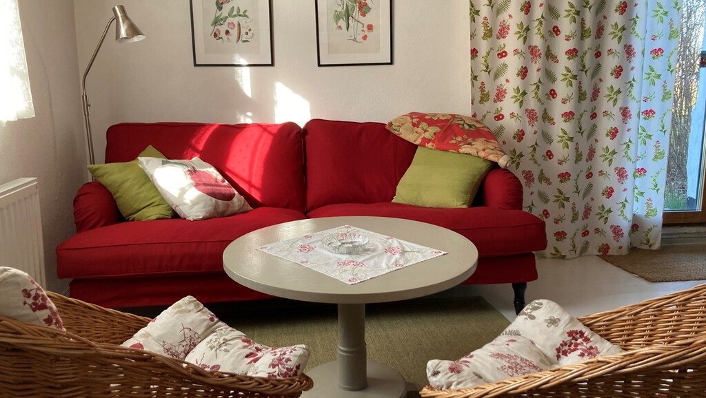 Röd soffa med kuddar, runt soffbord och rotting-fåtöljer i förgrunden
